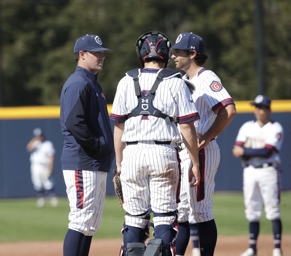 A coach talking with his catcher and pitcher on the field